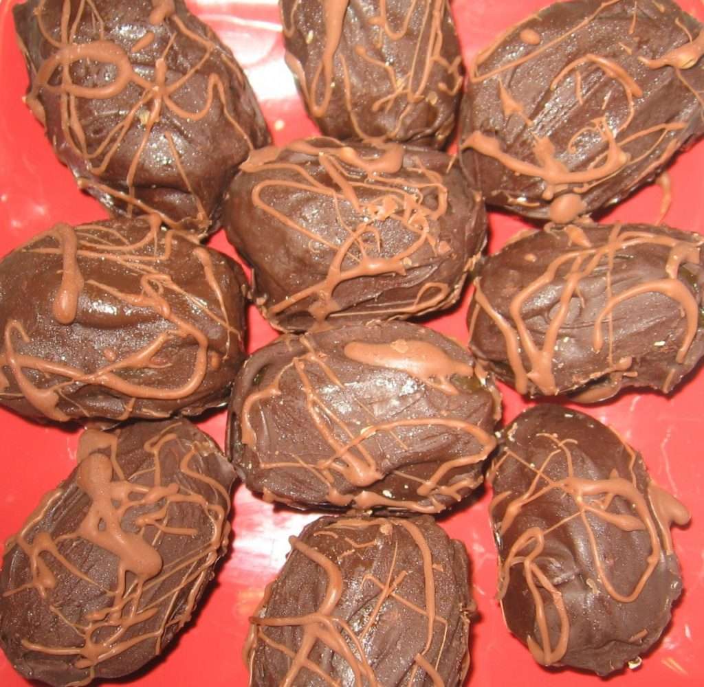 A red plate showcases chocolate-covered dates elegantly arranged in a circle. These plant-based treats are drizzled with more chocolate, creating an appetizing, textured appearance perfect for any vegan indulgence.