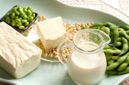 A plate showcasing plant-based goodness features a block of tofu, edamame in pods, a small pitcher of soy milk, green shelled edamame in a dish, and scattered soybeans. Perfectly curated for the vegan dietitian, this vibrant selection rests on a light-colored surface.