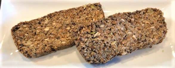 Two slices of seed loaf rest on a white rectangular plate. This dense, plant-based bread is packed with mixed seeds and grains, offering a textured look thats perfect for a vegetarian meal.