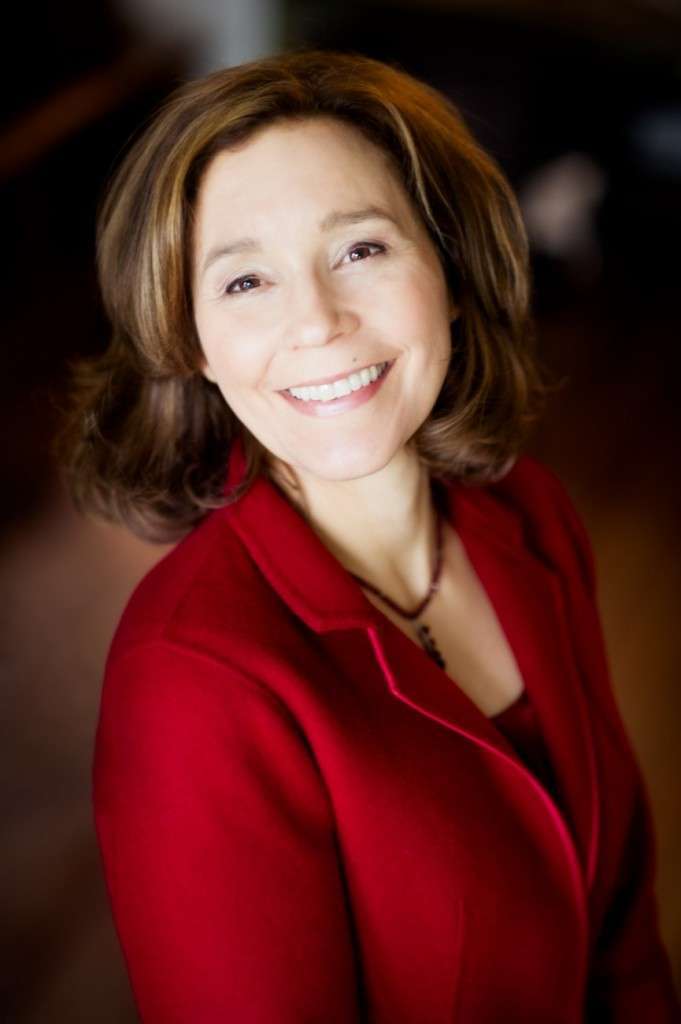 A person with shoulder-length brown hair is smiling while wearing a red jacket, exuding the warm expression of a dedicated dietitian. The softly blurred background complements her passion for promoting plant-based lifestyles.