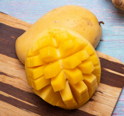 A ripe mango on a wooden surface, with one half peeled and cut into cubes, displaying its bright yellow flesh—a vibrant choice for any vegan. The other half of the mango is whole and has a smooth skin.