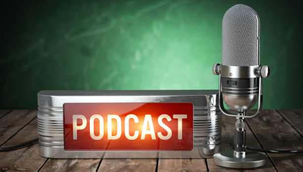A retro-style microphone stands next to a metallic sign displaying the word PODCAST in bold red letters. The background is a textured, dark green wall, and the surface is wooden.