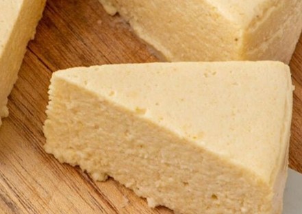 A close-up of a slice of soft, yellow cheesecake resting on a wooden surface, showing its smooth and creamy texture.