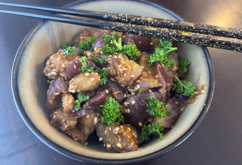 A bowl of marinated raw fish topped with sesame seeds and fresh parsley, with a pair of black and gold chopsticks resting on the bowls edge.