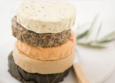 Four stacked rounds of cheese with various textures and colors, including herb-infused and smoked varieties.